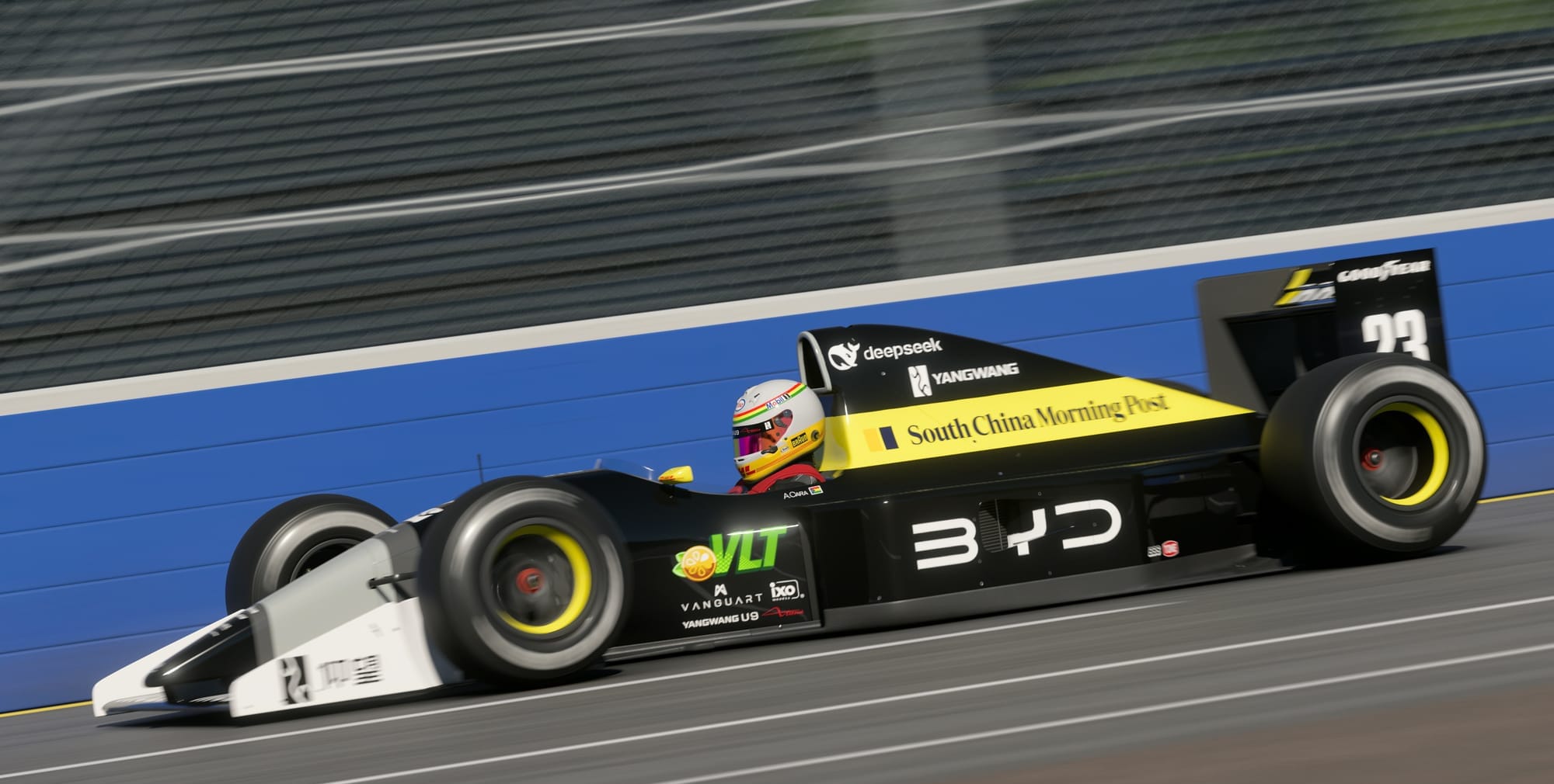 A black with grey and yellow open wheel race car that says BYD on the side at speed on a straightaway against a blue outside wall.