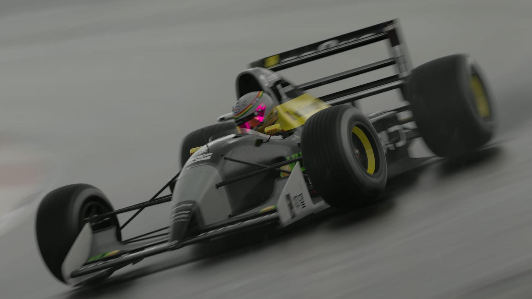 A black, with grey and yellow open wheel race car goes through a corner at speed.