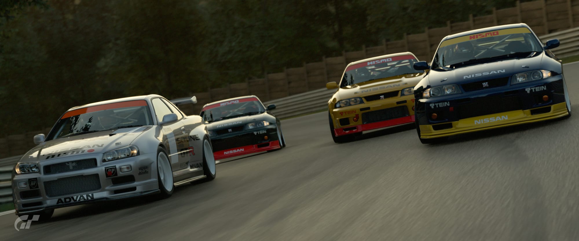A quartet of Nissan Skyline GT-Rs go through a right hand corner in close proximity, being led by a silver R34 and a blue and yellow R33. It is a screenshot from Gran Turismo 7.