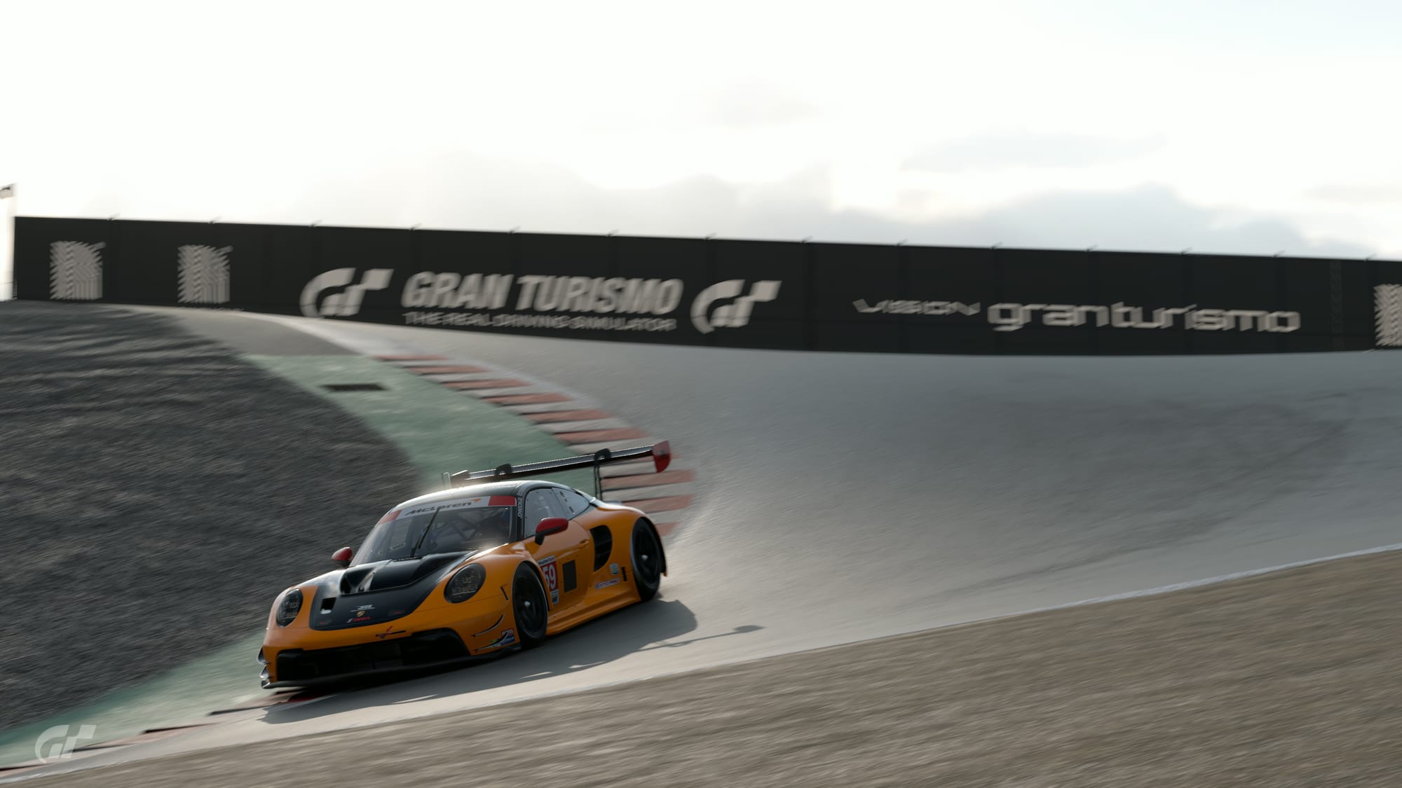A orange and black McLaren-branded Porsche 911 GT3 R goes through the corkscrew at Laguna Seca Raceway.
