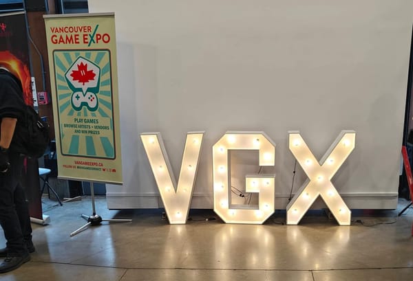 The VGX light up sign against a pull down projector wall, with the Vancouver Game Expo event banner alongside.